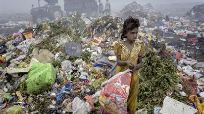 Ein Mädchen auf Abfallbergen mit einer Plastiktüte in der Hand, im Hintergrund eine Zugmaschine mit Hänger 