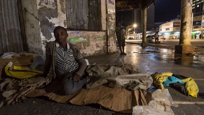 Kind sitzt an einer Straßenecke auf seinem Schlafplatz aus Pappe und Plastikfolien