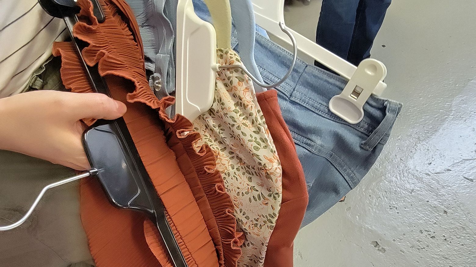 Eine Person, von der man nur eine Hand sieht, hält mehrer Kleidungsstücke