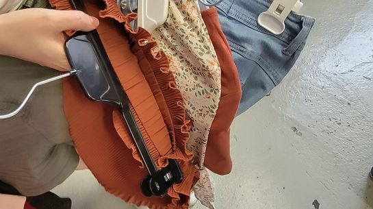 Eine Person, von der man nur eine Hand sieht, hält mehrer Kleidungsstücke