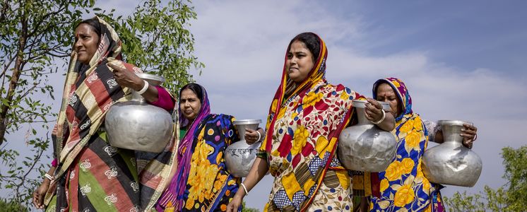 Frauen, wie hier Suparna Raptan (v.r.) aus der Umgebung von der Wasserstelle Vamia, tragen ihre Wasserkruege, die sie an der CCDB Wasserstelle Vamia gefuellt haben, nach Hause. Die Menschen in den kleinen Siedlungen an den Fluessen in der Naehe von Shyamnagar in Sued Bangladesch, spuehren deutlich den Klimawandel. Der Meeresspiegel steigt und Daemme werden zerstört. Da durch werden Felder und die wichtigen Suesswasserteiche ueberflutet und versalzen. CCDB Bangladesch arbeitet an Suesswassergewinnungs-Projekten und sorgt dafuer, dass die Menschen nach und nach sauberes Trinkwasser erhalten.