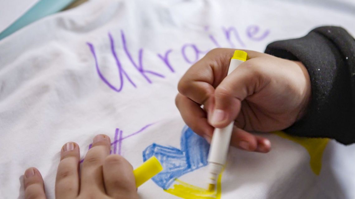 Ein Kind malt ein Herz mit den ukrainischen Farben Blau und Gelb.