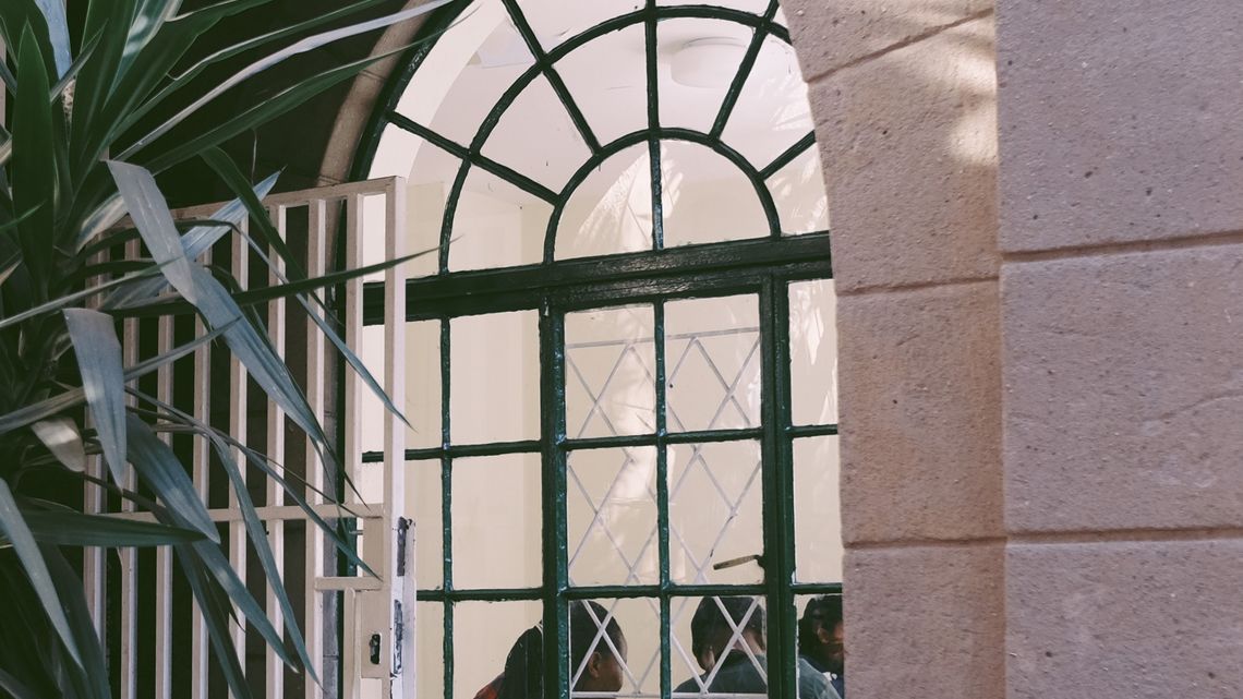 "People on the Move erhalten Sprachunterricht hinter einem vergitterten Fenster"