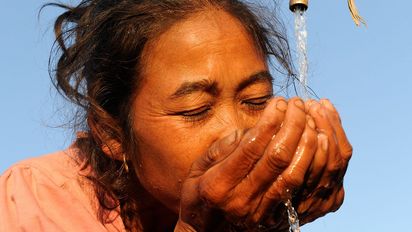 Eine asiatische Frau trinkt Wasser von einem Wasserhahn.