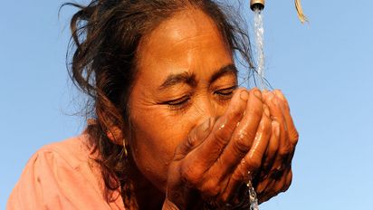 Eine asiatische Frau trinkt Wasser von einem Wasserhahn.