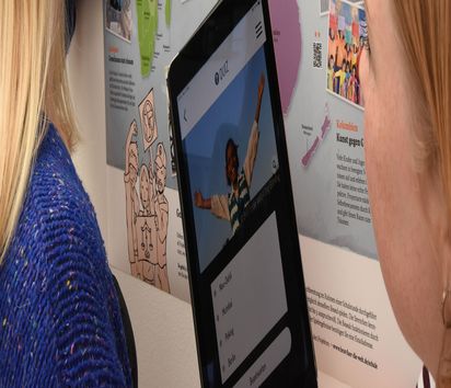 Zwei Mädchen vor einer Weltkarte mit einem Tablet auf dem ein Quiz zu lösen ist