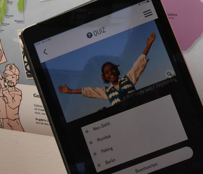 Zwei Mädchen vor einer Weltkarte mit einem Tablet auf dem ein Quiz zu lösen ist