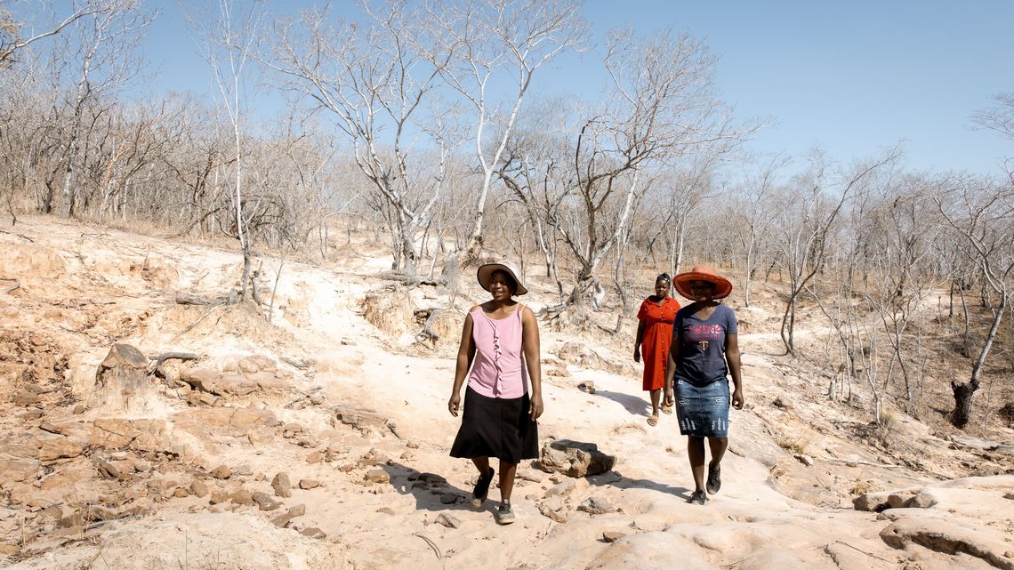 Die Freundinnen Beauty Nyathi (45), Gracious Mujuma (42) und Sihle Hahlani (31) gehen durch karge, trockene Landschaft zum nahegelegenen Fluss. Durch MeDRAs Arbeit (BfdW-Partnerorganisation) hat sich ihr Leben sehr verbessert. Sie lernen und unterstuetzen sich gegenseitig.