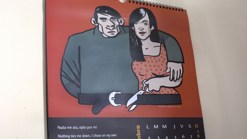 Ein Kalender hängt an der Wand. Das Kalenderbild zeigt eine Frau die den Gürtel des Mannes durchschneidet.