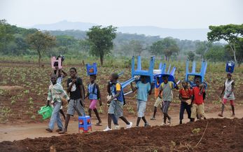 In Angola tragen Kinder Plastikstühle auf dem Weg zur Schule 