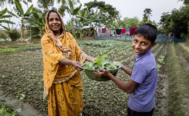 Mutter und Sohn halten selbst geerntetes Gemüse auf ihrem Feld in Bangladesch in den Händen.