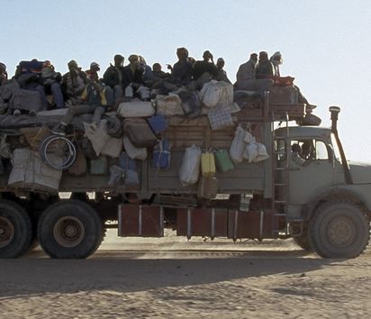 Ein Lastwagen der mit Menschen und Gepäck beladen ist fährt durch die Wüste