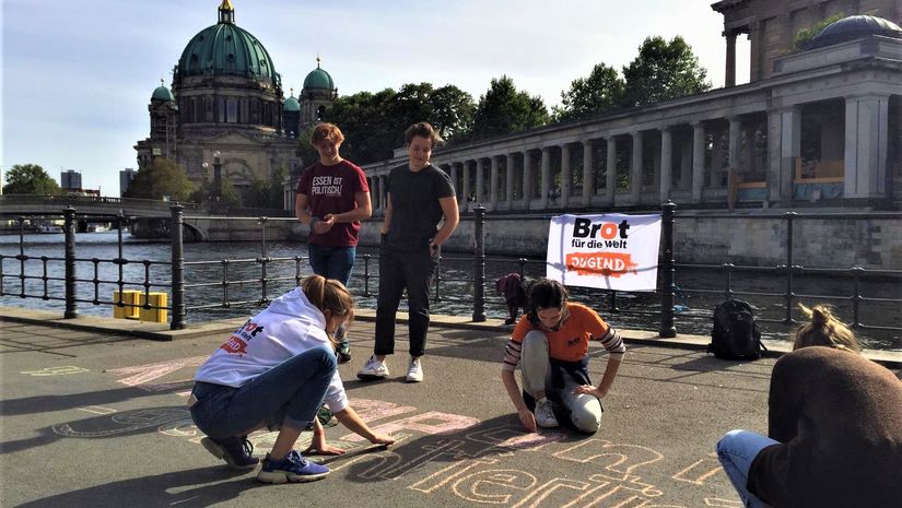 Brot für die Welt Jugend schreibt mit Kreide Botschaften auf die Straße, Berliner Dom im Hintergrund