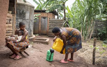 ACORD beneficiaries Immaculate Amatwire, 17, holds her little brother Levison Kamugiso, three months old, as their mother Kamusiime Joy, 38, prepares to water their vegetable garden at their home in Kikunda 1 village, Rwampara District, western Uganda, on January 29, 2025.
