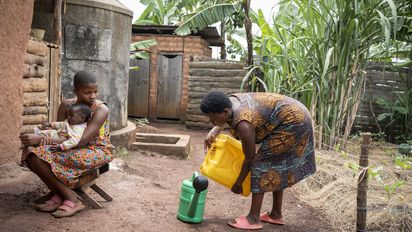 ACORD beneficiaries Immaculate Amatwire, 17, holds her little brother Levison Kamugiso, three months old, as their mother Kamusiime Joy, 38, prepares to water their vegetable garden at their home in Kikunda 1 village, Rwampara District, western Uganda, on January 29, 2025.