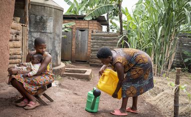 ACORD beneficiaries Immaculate Amatwire, 17, holds her little brother Levison Kamugiso, three months old, as their mother Kamusiime Joy, 38, prepares to water their vegetable garden at their home in Kikunda 1 village, Rwampara District, western Uganda, on January 29, 2025.