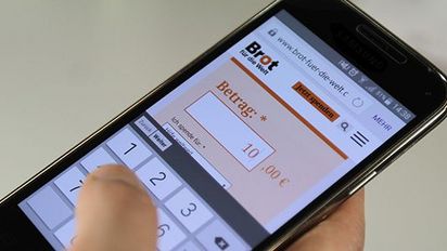 Eine Hand hält ein Handy in der Hand. Auf dem bildschirm ist eine BfdW Spendenbox zu sehen. Der Eingetragene Betrag ist 10€.