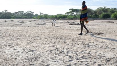 Mann in traditioneller Kleidung der Turkana Volksgruppe läuft über ein ausgetrocknetes Flussbett