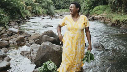 Luisa Curuki steht lachend im Fluss und hält Bele-Blätter in der Hand.