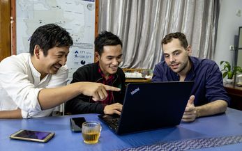 Drei Menschen sitzen an einem Laptop und diskutieren fröhlich