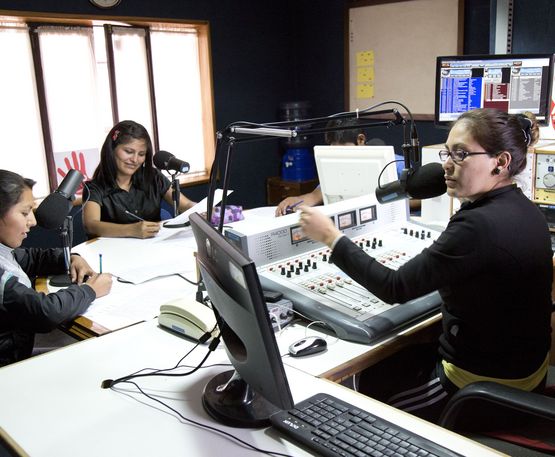 eine Frau am Mischpult des Radiosenders und drei Leute an Mikrofonen