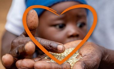 Hand hält Hirse, im Hintergrund das Gesicht eines Babys, das in ein Herz gerahmt ist.