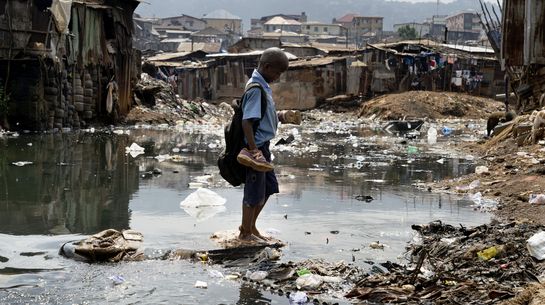 Ein SChuljunge im Slum Kroo Bay in Sierra Leone versucht trotz Grauwasserpfützen trockenen Fusses nach Hause zu kommen