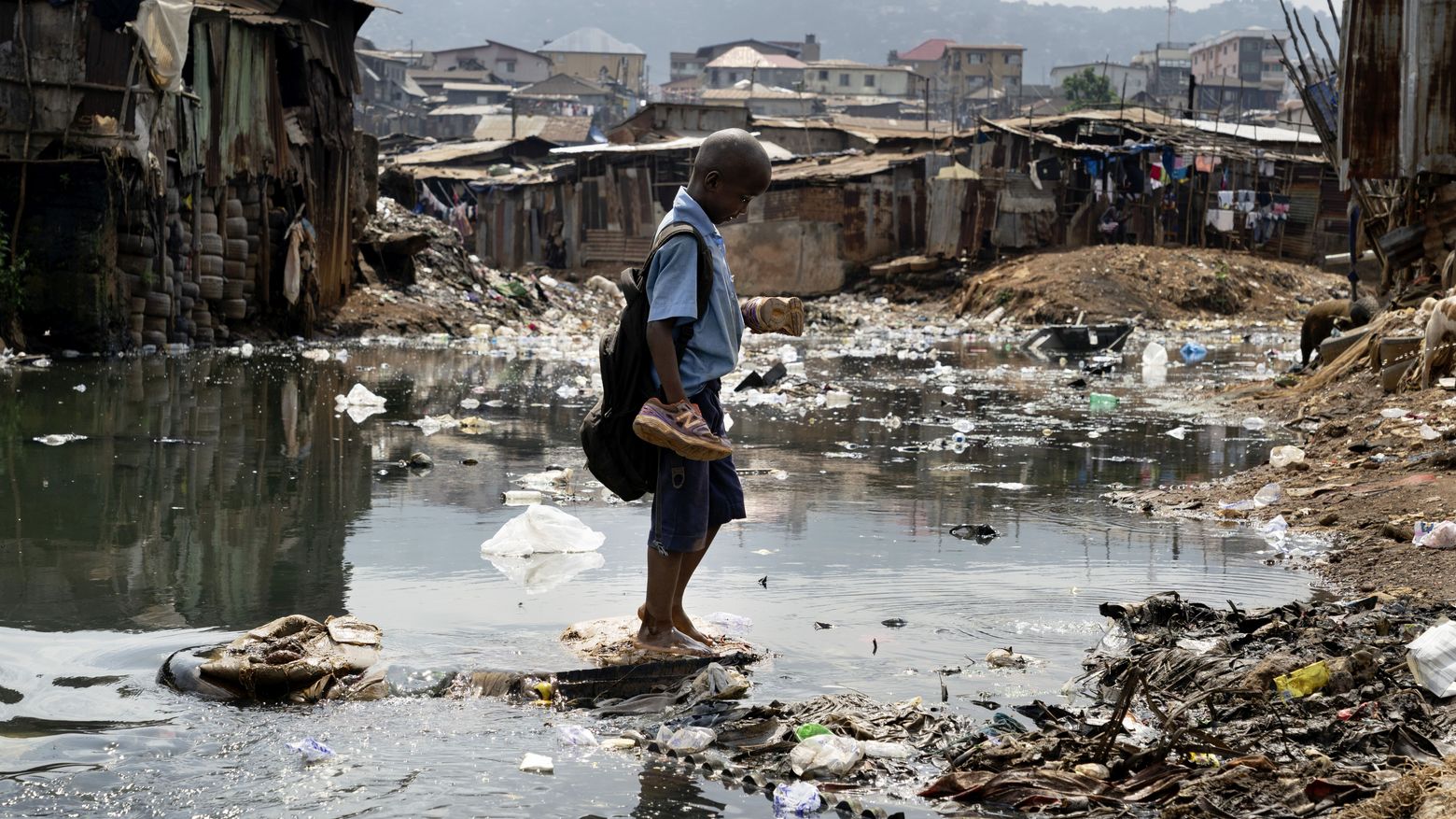 Ein SChuljunge im Slum Kroo Bay in Sierra Leone versucht trotz Grauwasserpfützen trockenen Fusses nach Hause zu kommen