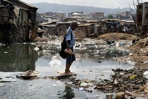 Ein SChuljunge im Slum Kroo Bay in Sierra Leone versucht trotz Grauwasserpfützen trockenen Fusses nach Hause zu kommen