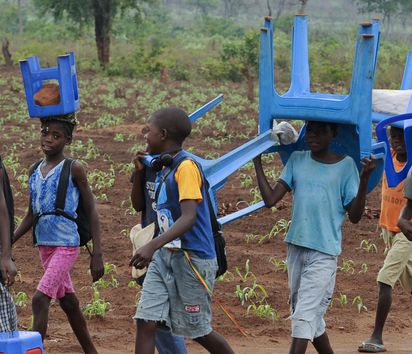In Angola tragen Kinder Plastikstühle auf dem Weg zur Schule 