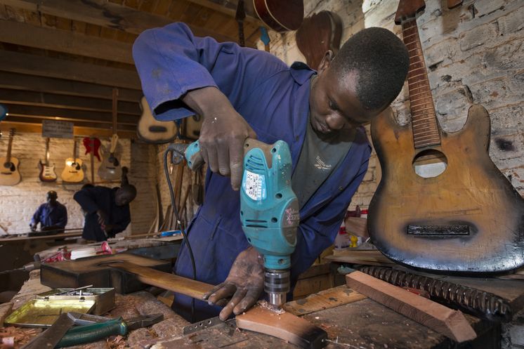Der Gitarrenbauer Justin Murhula Bashimbe bohrt am Kopf der Gitarre die Löcher für die Stimmmechanik