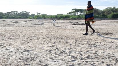 Mann in traditioneller Kleidung der Turkana Volksgruppe läuft über ein ausgetrocknetes Flussbett