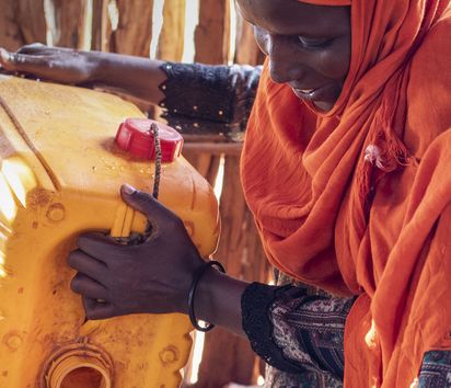 Fatuma Abdullhai gießt Wasser aus einem Plastik Kanister in einen Topf
