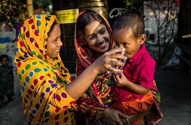 CCDB Bangladesch Sayra Begum (m.), profitiert von ihrer Regenwassergewinnung, die von CCDB gestellt wurde und kann jetzt sauberes Trinkwasser aus dem Wassertank zapfen und ihrem Sohn geben. Die Menschen in den kleinen Siedlungen an den Fluessen in der Naehe von Shyamnagar in Sued Bangladesch, spuehren deutlich den Klimawandel. Der Meeresspiegel steigt und Daemme werden zerstört. Da durch werden Felder und die wichtigen Suesswasserteiche ueberflutet und versalzen. CCDB Bangladesch arbeitet an Suesswassergewinnungs-Projekten und sorgt dafuer, dass die Menschen nach und nach sauberes Trinkwasser erhalten.