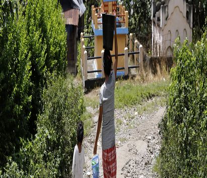 Mutter, die einen Eimer trägt und Kind laufen den Berg hinab.