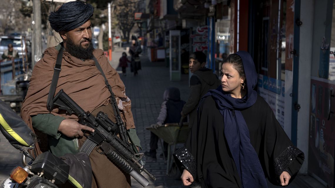 FILE - A Taliban fighter stands guard as a woman walks past in Kabul, Afghanistan, on Dec. 26, 2022. The United Nations' human rights chief on Tuesday Dec. 27, 2022 decried increasing restrictions on women's rights in Afghanistan, urging the country's Taliban rulers to reverse them immediately. He pointed to “terrible consequences” of a decision to bar women from working for non-governmental organizations. (AP Photo/Ebrahim Noroozi, File)