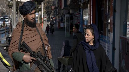 FILE - A Taliban fighter stands guard as a woman walks past in Kabul, Afghanistan, on Dec. 26, 2022. The United Nations' human rights chief on Tuesday Dec. 27, 2022 decried increasing restrictions on women's rights in Afghanistan, urging the country's Taliban rulers to reverse them immediately. He pointed to “terrible consequences” of a decision to bar women from working for non-governmental organizations. (AP Photo/Ebrahim Noroozi, File)