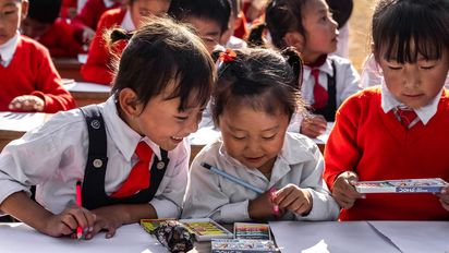 Asiatische Schulkinder schreiben mit Stiften auf Blättern.