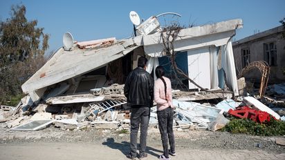 Ehepaar steht vor dem vom Erdbeben zerstörten Haus in Hatay