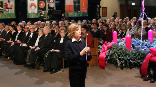 Ein Junge entzündet die erste Kerze am Adventskranz.