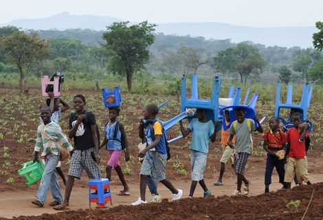 In Angola tragen Kinder Plastikstühle auf dem Weg zur Schule 