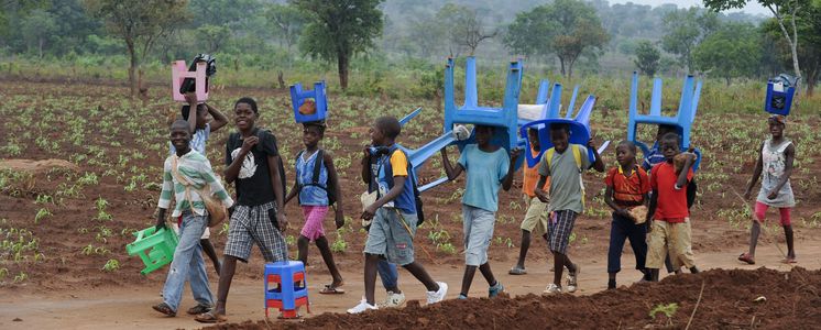 In Angola tragen Kinder Plastikstühle auf dem Weg zur Schule 