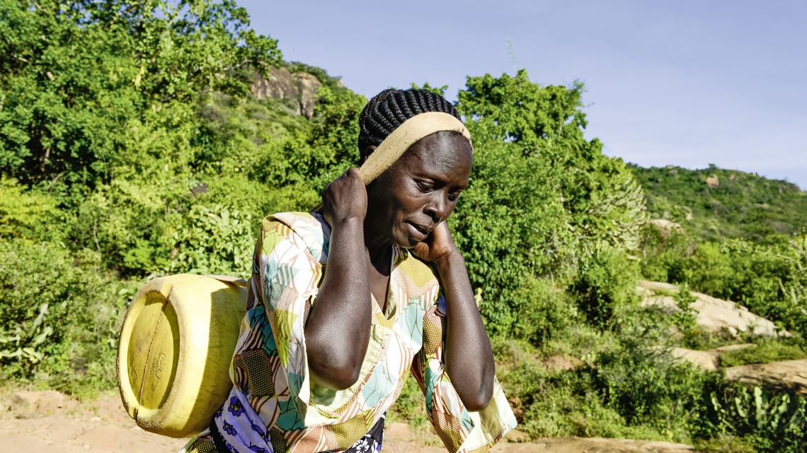 KENIA, ADS Anglican Development Services of Mount Kenya East, Stadt Embu, Dorf Gichunguri, Projekt Regenwasserauffang an einem Felsen und Speicherung in Tanks zur Nutzung in Duerreperioden, Agnes Irima, 44 Jahre, traegt einen gefuellten Wasserkanister nach Hause, ca. 200 Meter