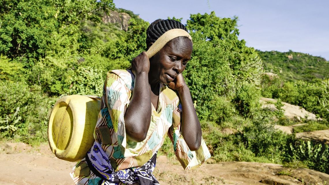KENIA, ADS Anglican Development Services of Mount Kenya East, Stadt Embu, Dorf Gichunguri, Projekt Regenwasserauffang an einem Felsen und Speicherung in Tanks zur Nutzung in Duerreperioden, Agnes Irima, 44 Jahre, traegt einen gefuellten Wasserkanister nach Hause, ca. 200 Meter