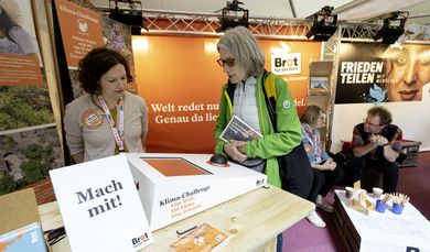 Besucher des 102. Deutschen Katholikentags am Brot-fuer-die-Welt Stand im Gespraech mit den Mitarbeitern von Brot fuer die Welt.