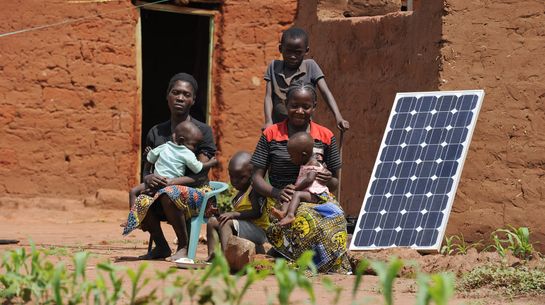 Familie mit Solarpanel zur Stromversorgung ihrer Lehmhütte