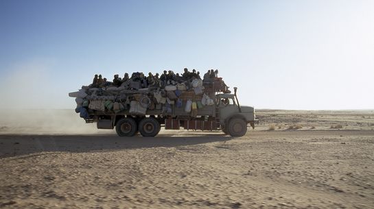 Mit Menschen voll besetzter LKW fährt durch Wüste