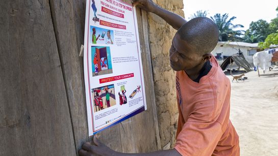 Ein Mann klebt ein Plakat mit Hygiene-Regeln an die Wand.