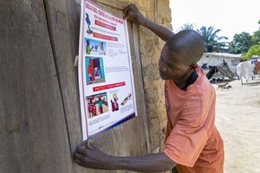 Ein Mann klebt ein Plakat mit Hygiene-Regeln an die Wand.