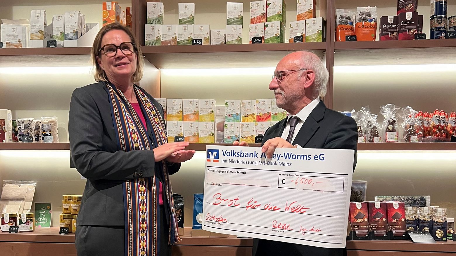 Auf dem Bild sind zwei Personen zu sehen. Die rechts stehende Person hält einen übergroßen Spendenscheck in den Händen, der auf den Betrag von 6.500 Euro aufgestellt ist.